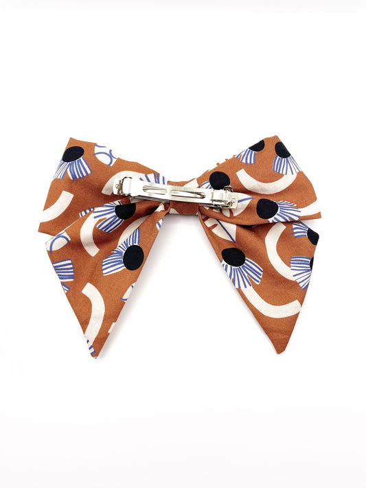 A large handmade hair bow with an abstract floral and leaf print in cream, black, and soft blue. The cotton fabric is attached to a sturdy barrette clip.