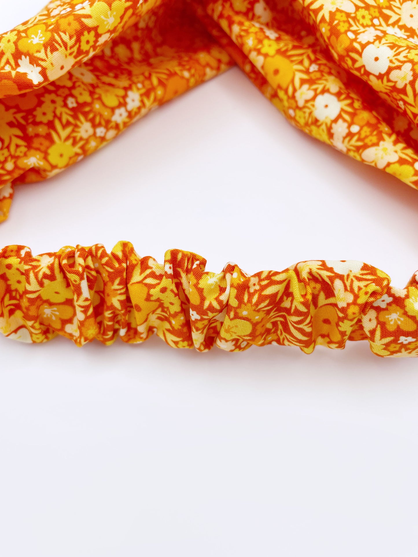 An orange cotton twist headband with a colorful ditsy floral print. The headband has an elastic band in the back to provide comfort without slipping.