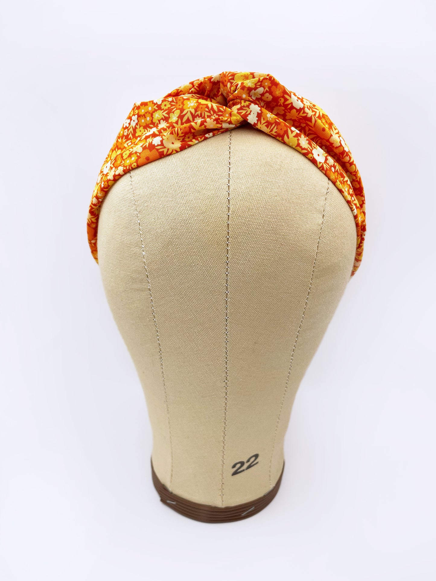 An orange cotton twist headband with a colorful ditsy floral print shown on a mannequin head.