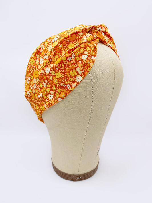 An orange cotton twist headband with a colorful ditsy floral print shown on a mannequin head.