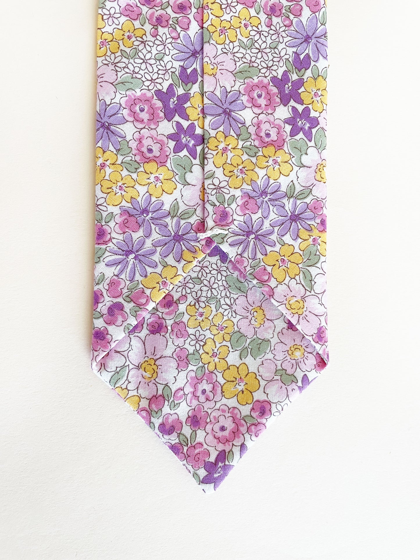 A handmade purple floral necktie against an off white background.