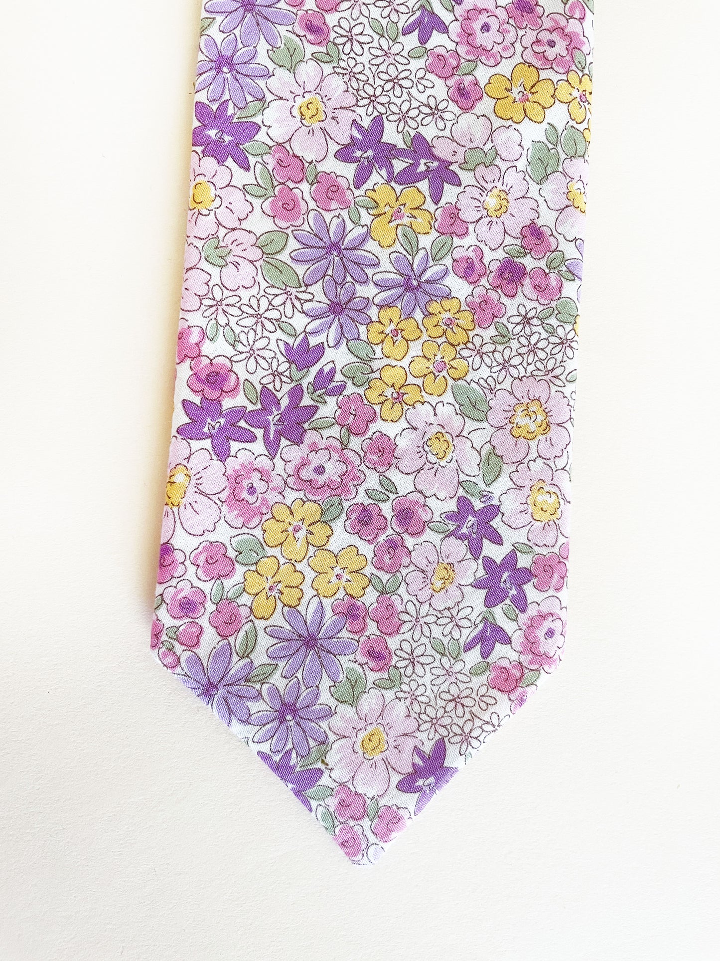 A handmade purple floral necktie against an off white background.