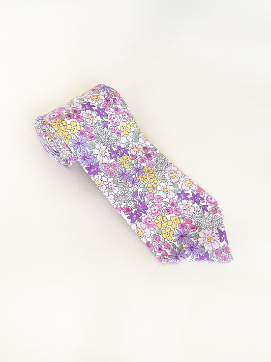 A handmade purple floral necktie against an off white background.