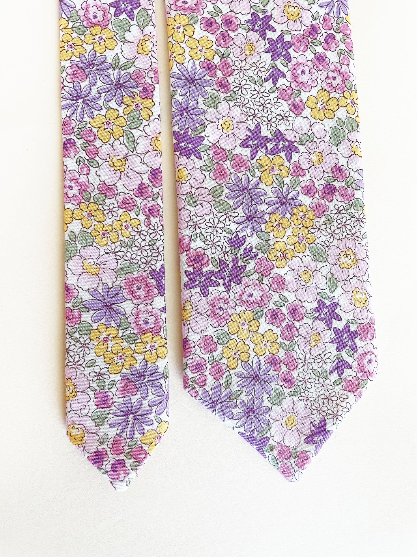 A handmade purple floral necktie against an off white background.