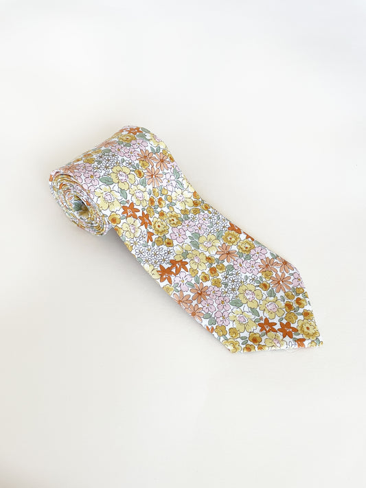 A handmade yellow floral necktie against an off white background.