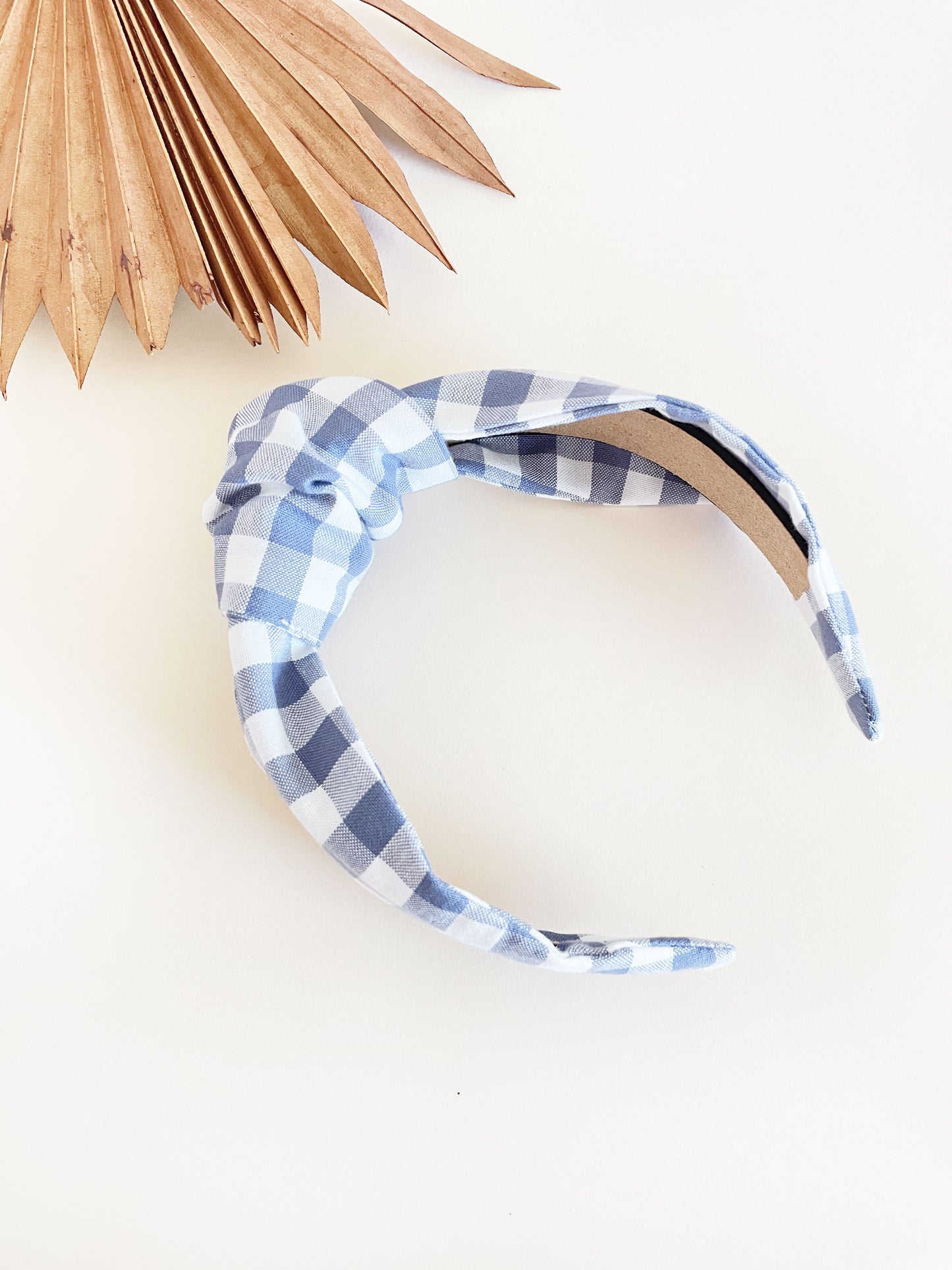 A handmade slate blue gingham plaid knotted headband against an off white background.