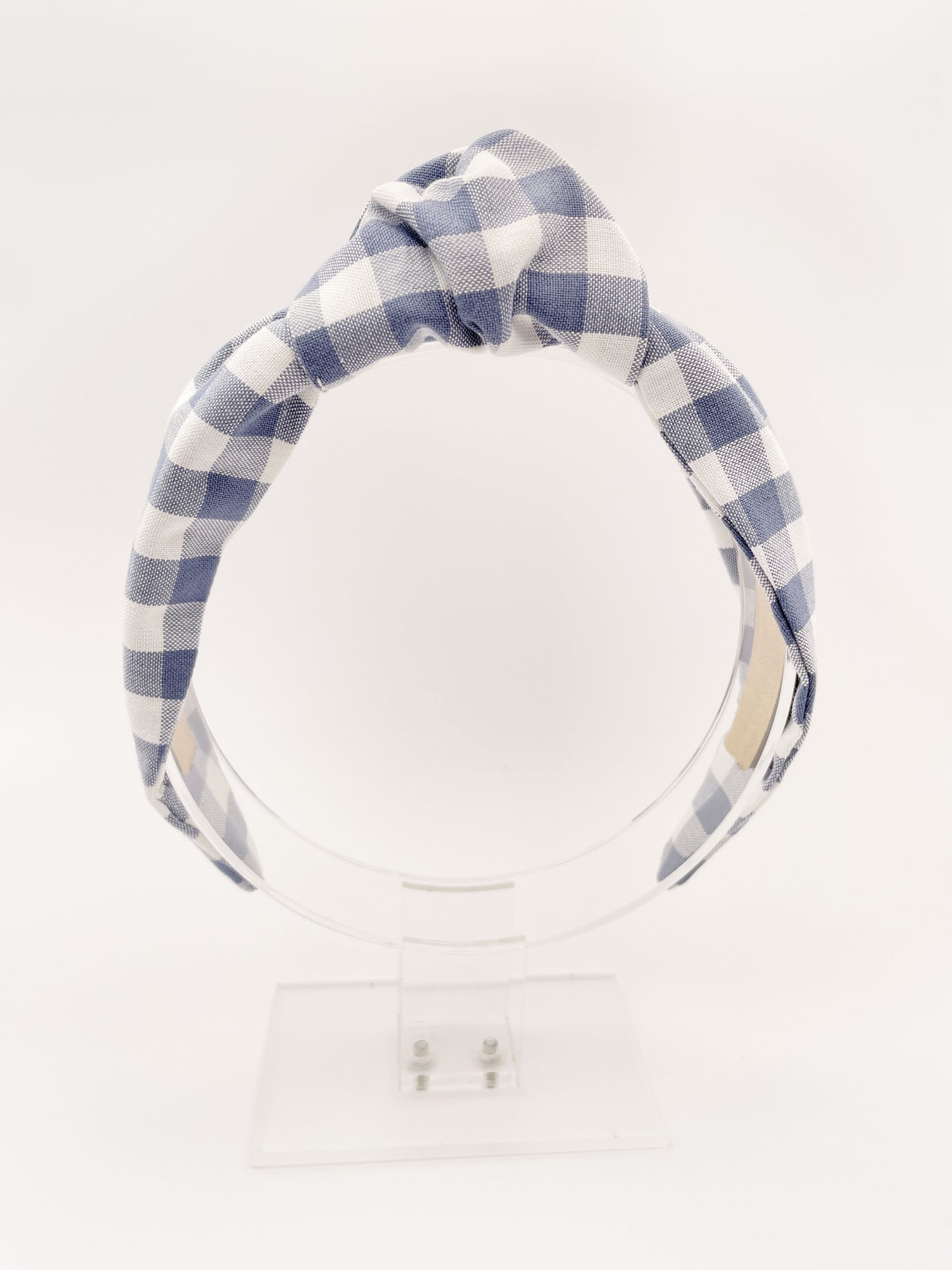 A handmade slate blue gingham plaid knotted headband against an off white background.