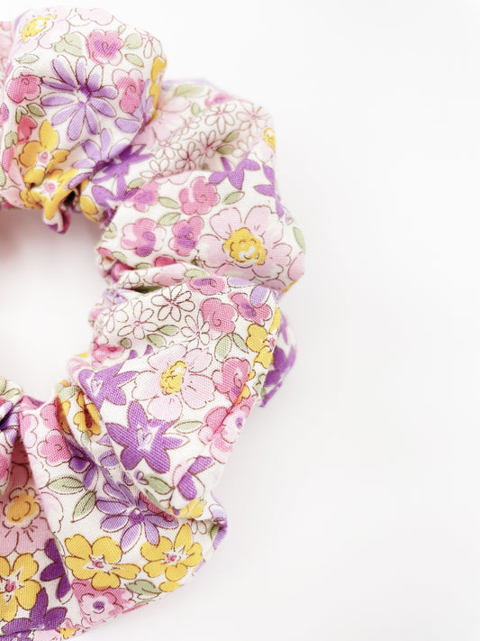 A handmade purple floral scrunchie against an off white background.
