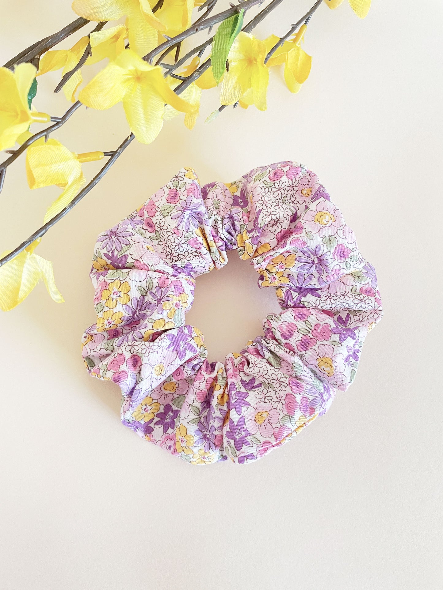 A handmade purple floral scrunchie against an off white background.