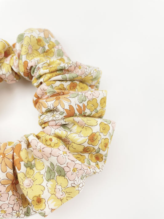 A handmade boho yellow floral scrunchie against an off white background.