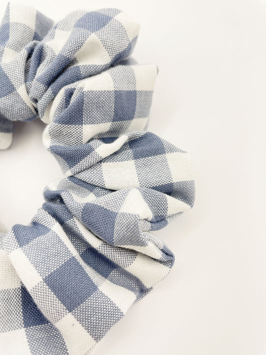 A handmade slate blue gingham plaid scrunchie against an off white background.