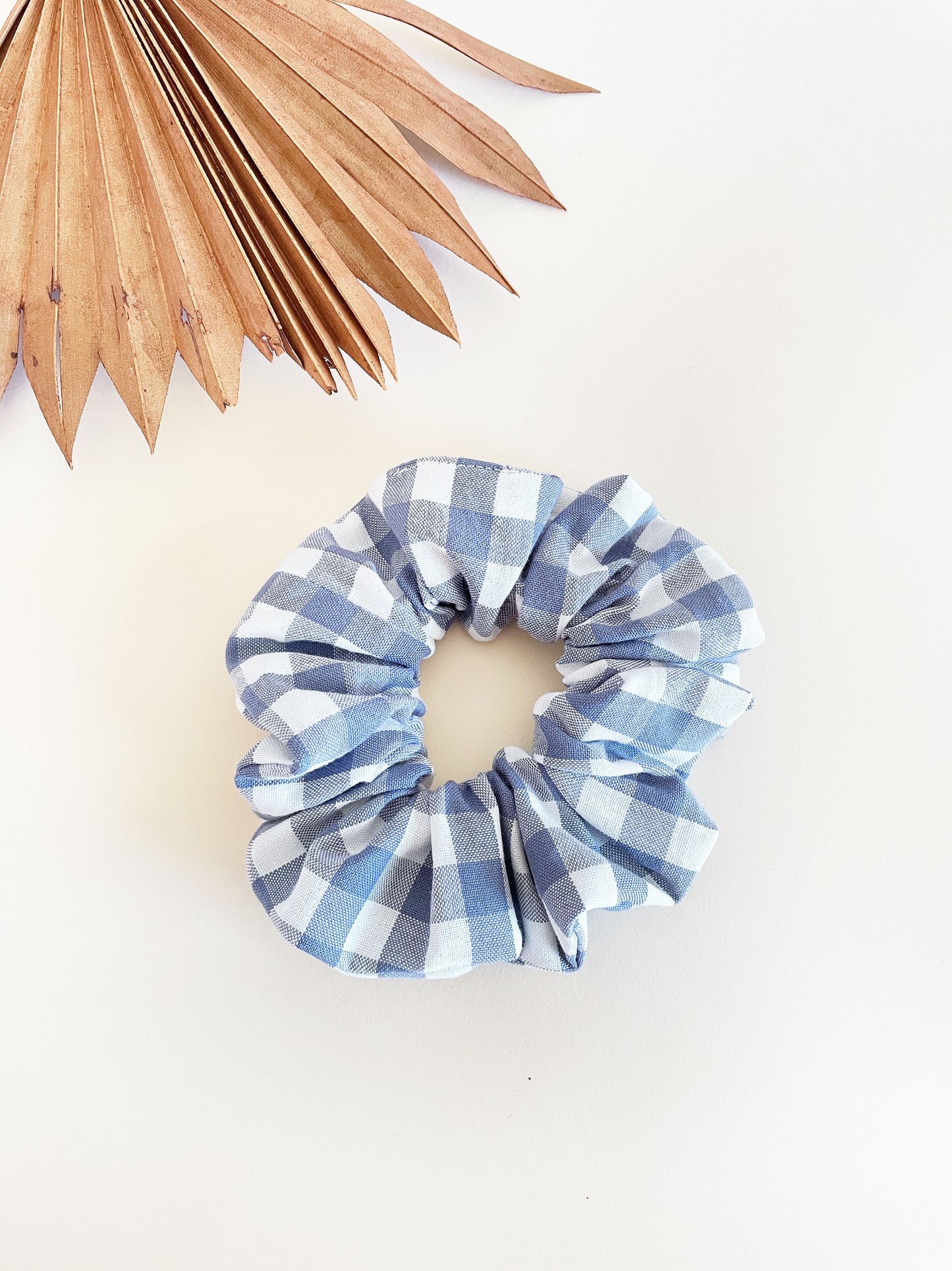 A handmade slate blue gingham plaid scrunchie against an off white background.