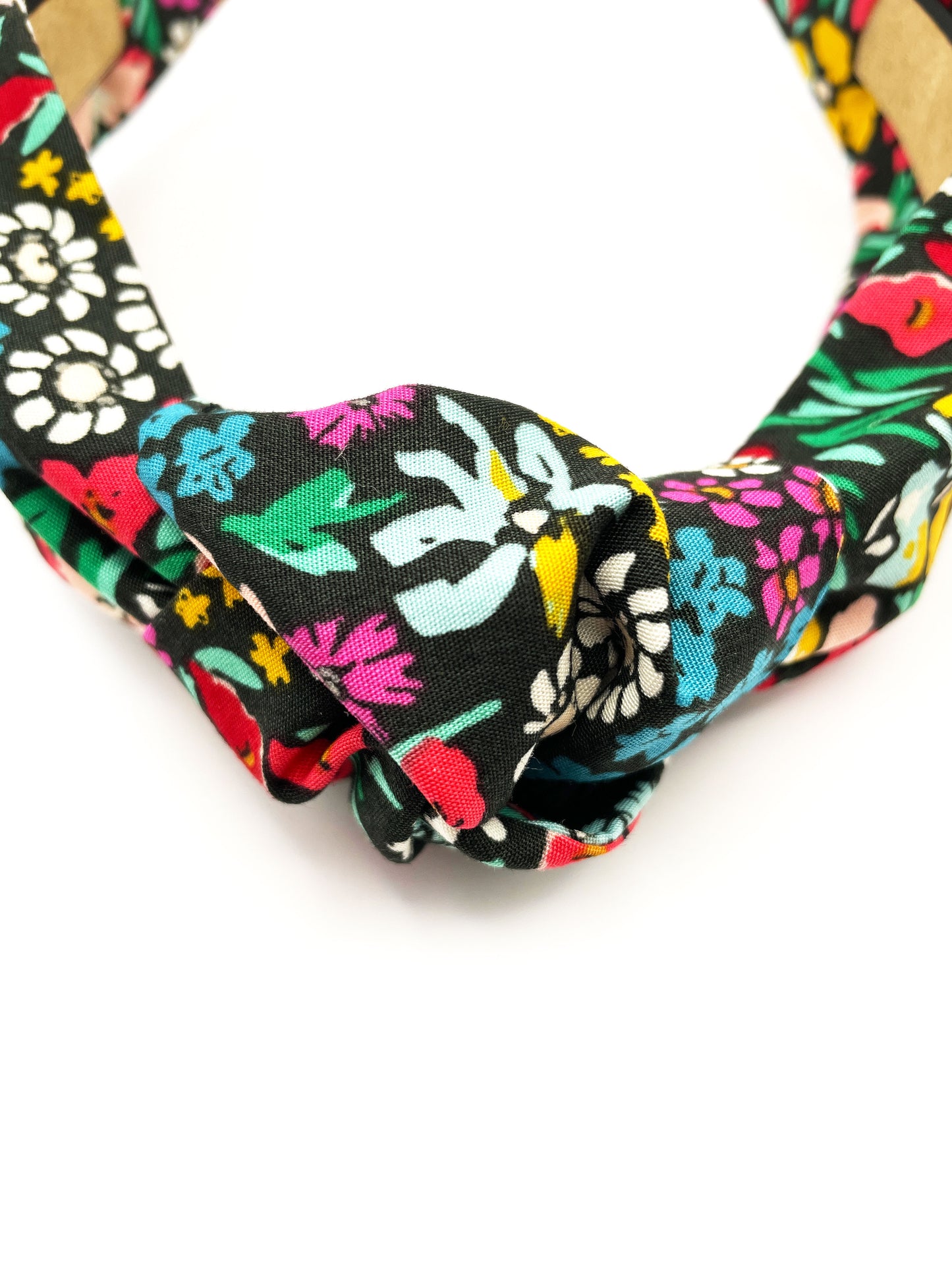 A black handmade knotted headband with a colorful floral print.