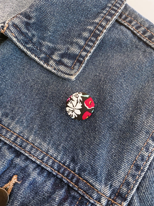 Handmade black floral fabric covered lapel pin on a denim jacket.