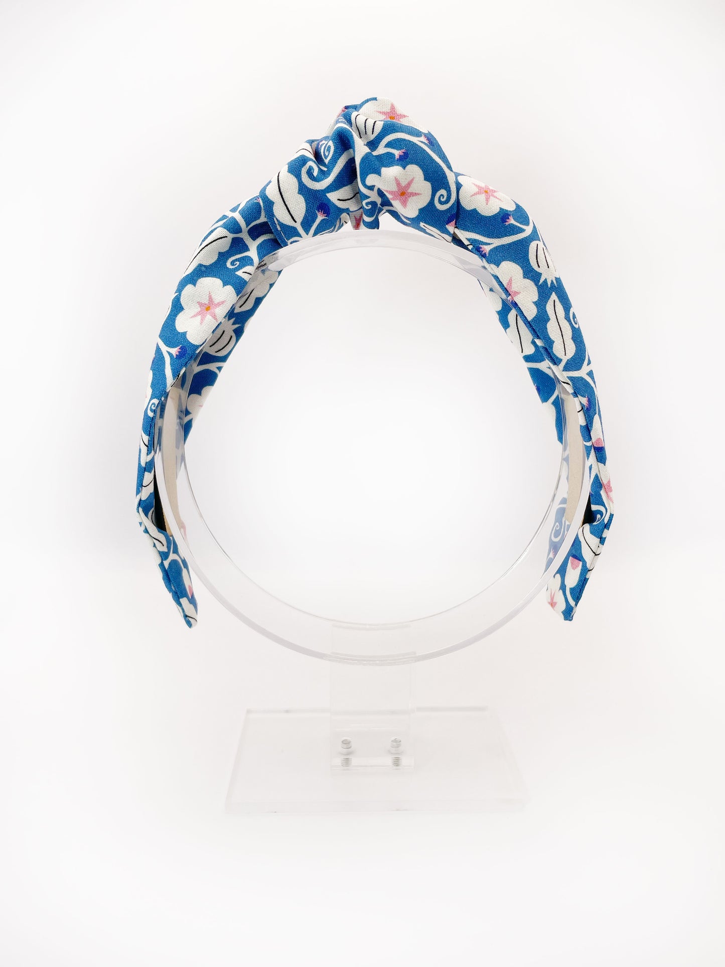 A blue knotted headband with white flowers that have pink centers.