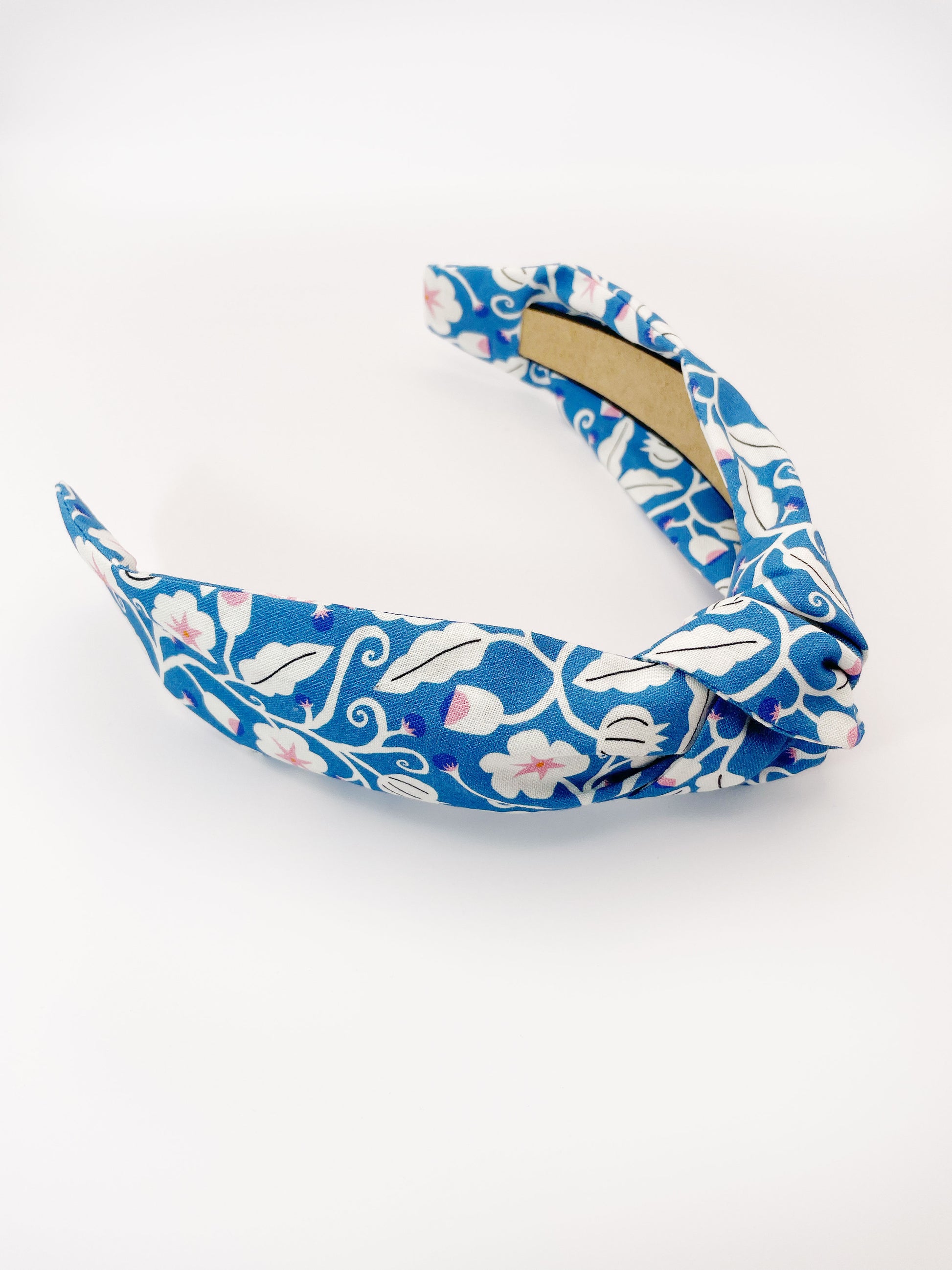 A blue knotted headband with white flowers that have pink centers.