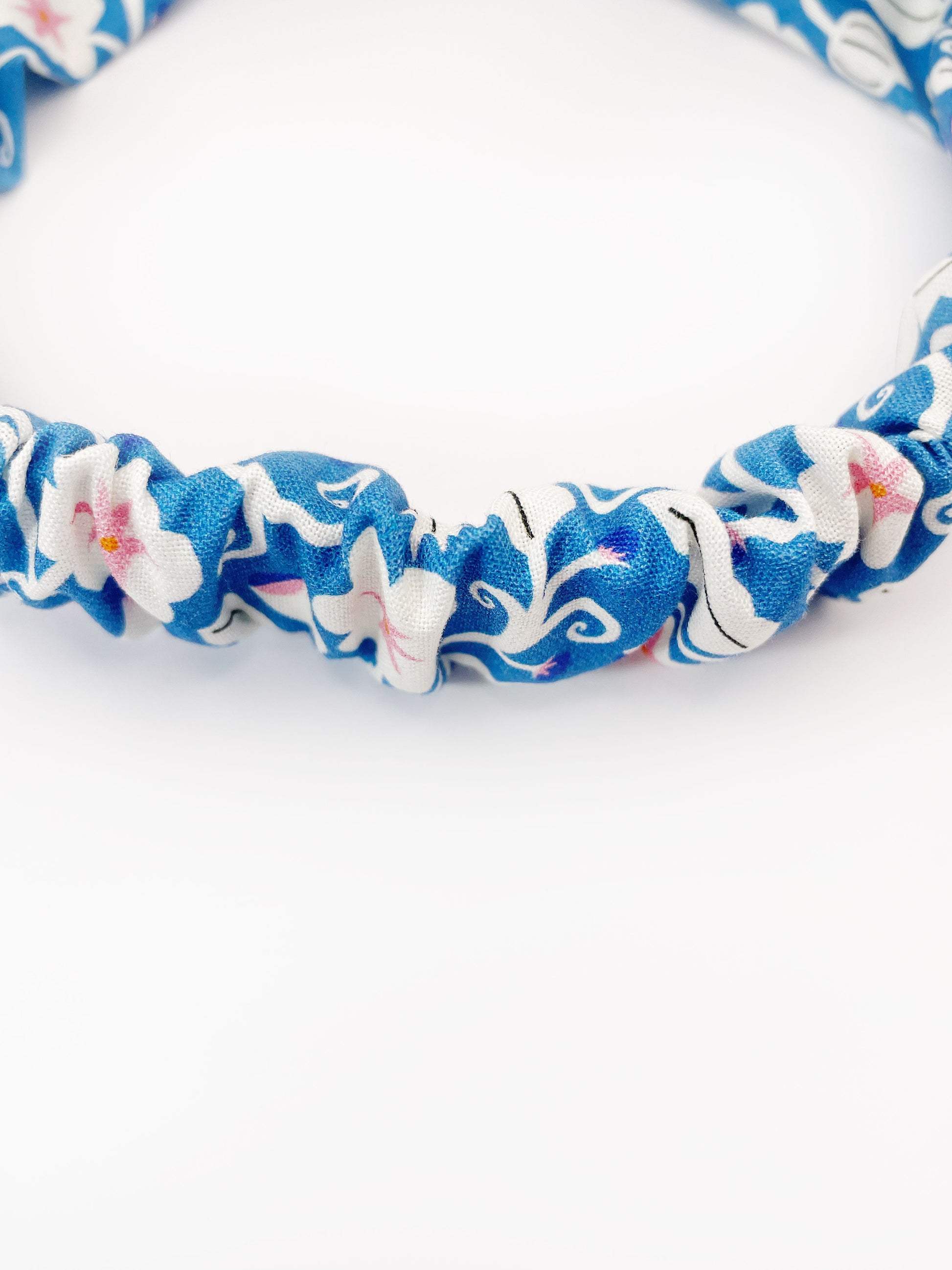 A blue twist headband with white flowers that have pink centers. The elastic band in the back provides support without slipping.