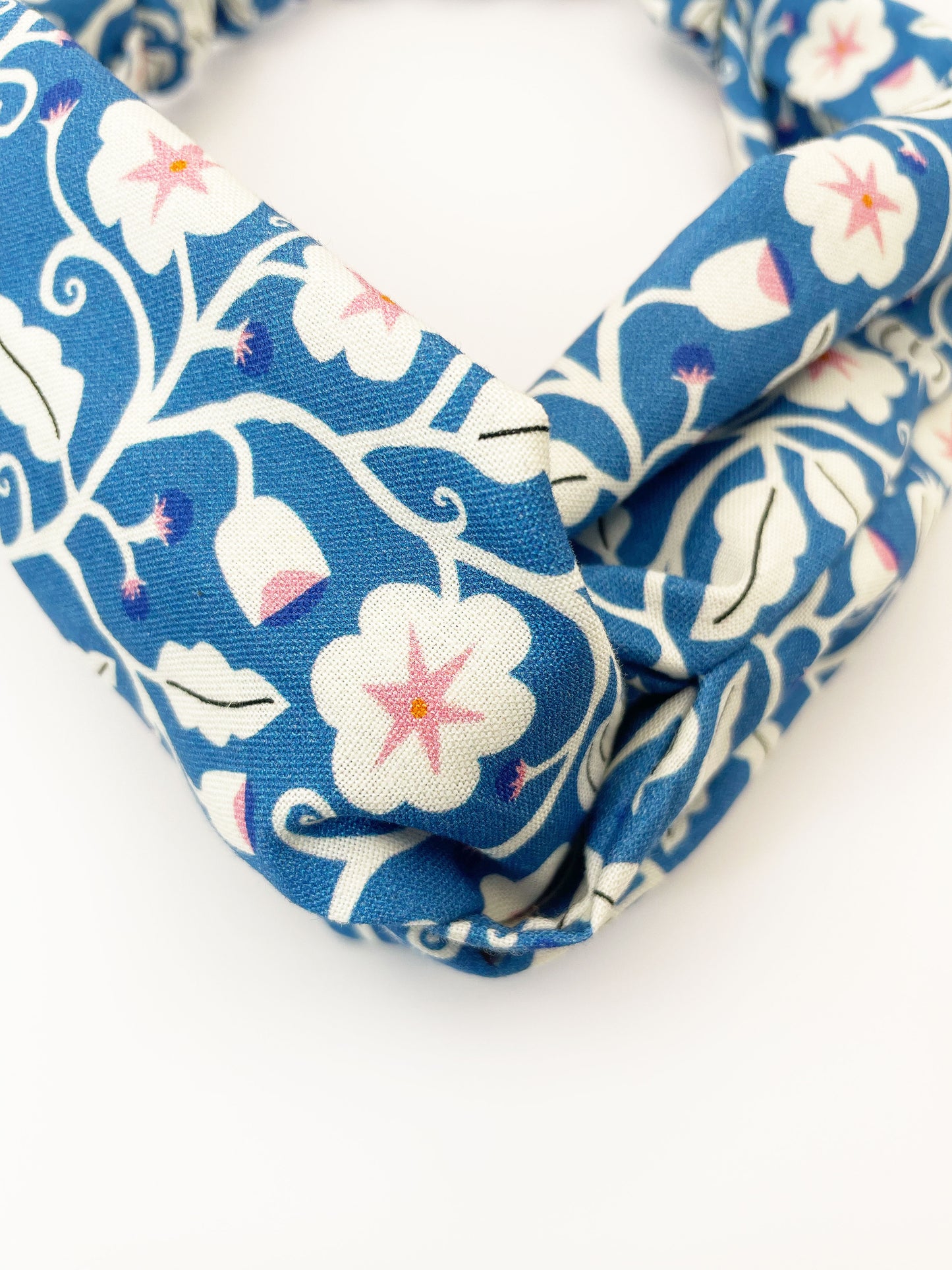 A blue twist headband with white flowers that have pink centers.