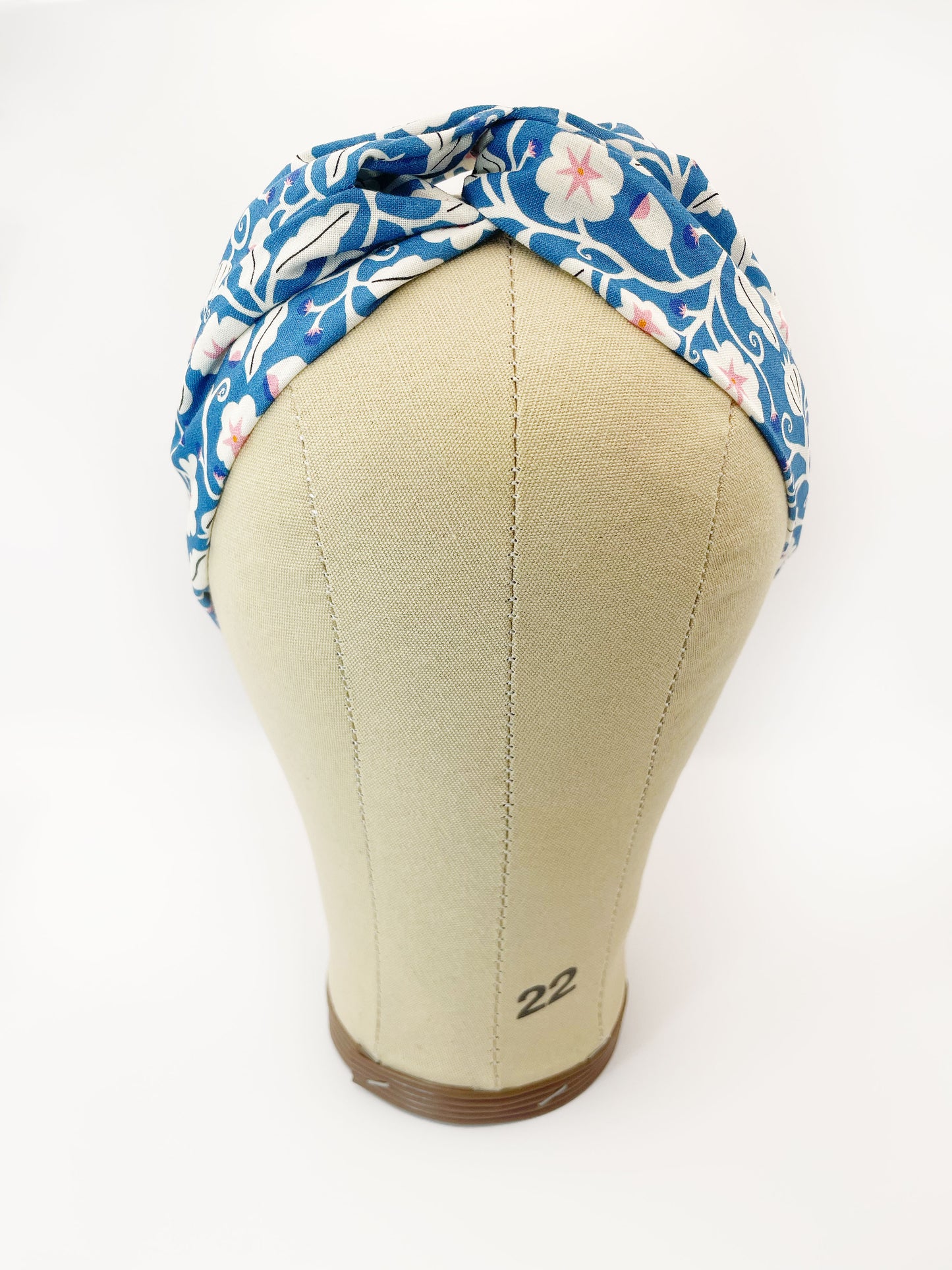 A blue twist headband with white flowers that have pink centers. The headband is modeled on a mannequin head.