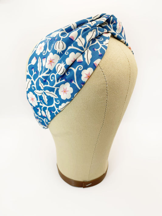 A blue twist headband with white flowers that have pink centers. The headband is modeled on a mannequin head.