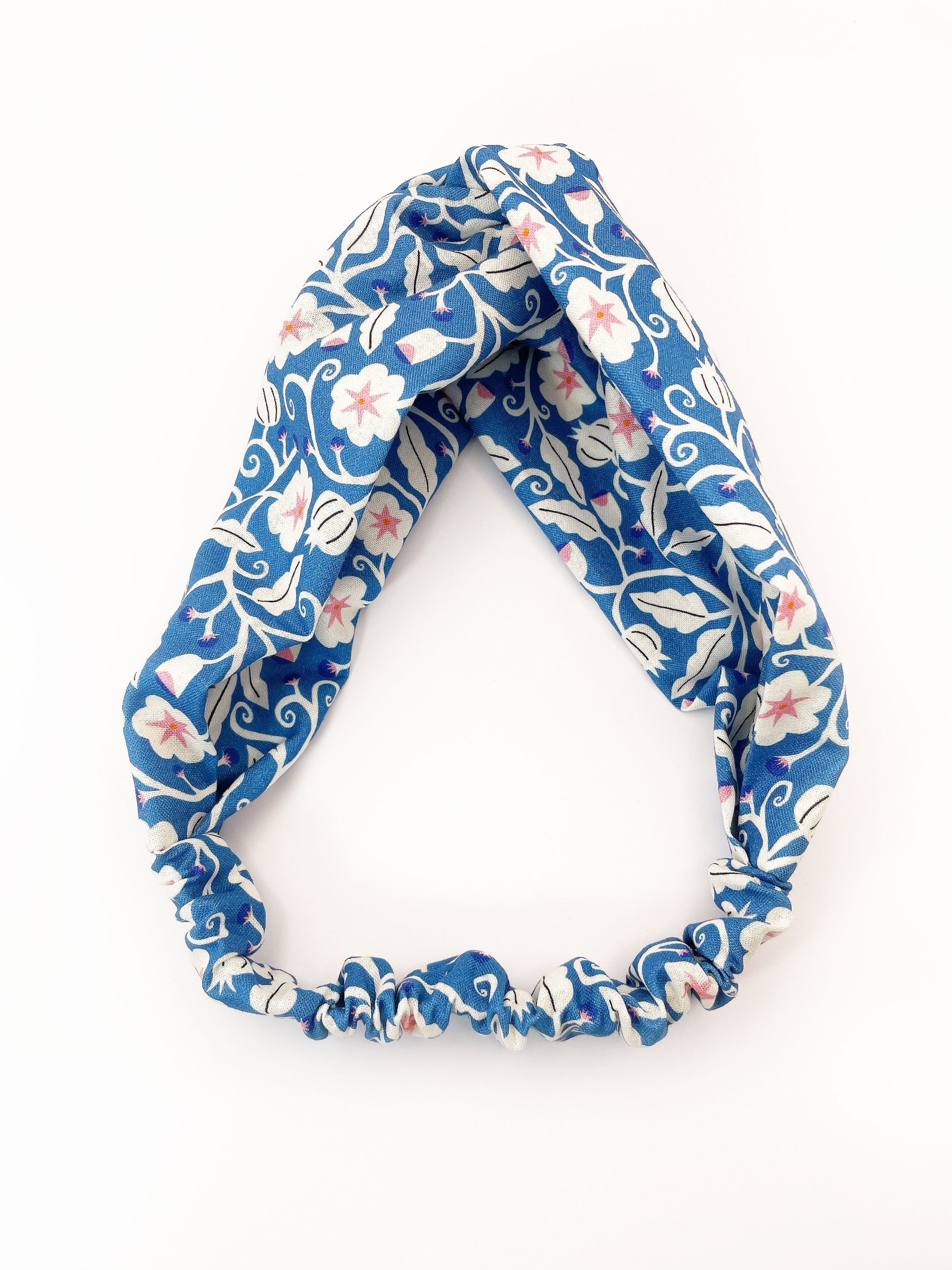 A blue twist headband with white flowers that have pink centers. The elastic band in the back provides support without slipping.