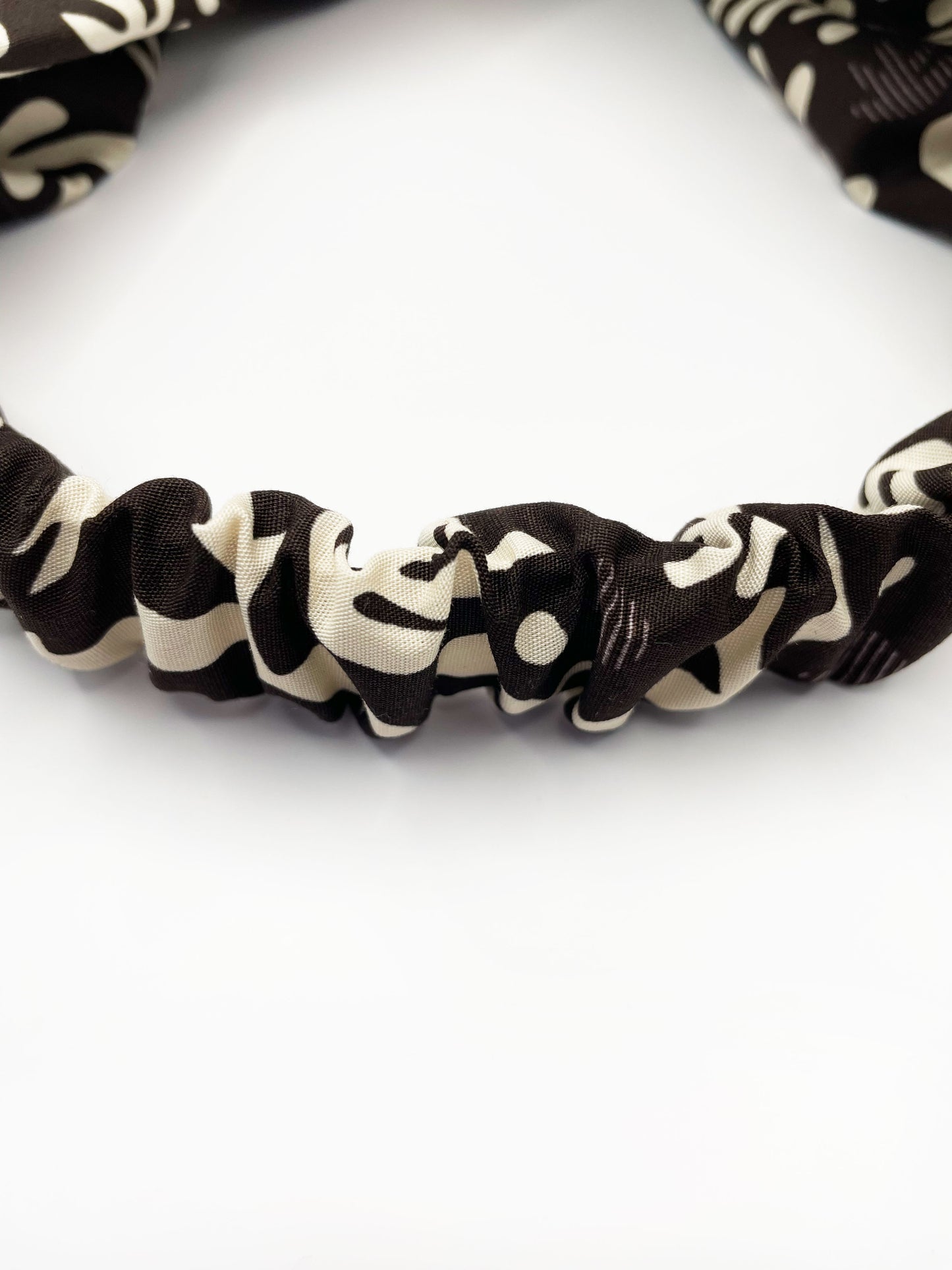 A dark charcoal gray twist headband with cream-colored birds and abstract shapes. The elastic band in the back provides support without slipping.