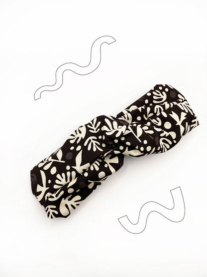 A dark charcoal gray twist headband with cream-colored birds and abstract shapes. 