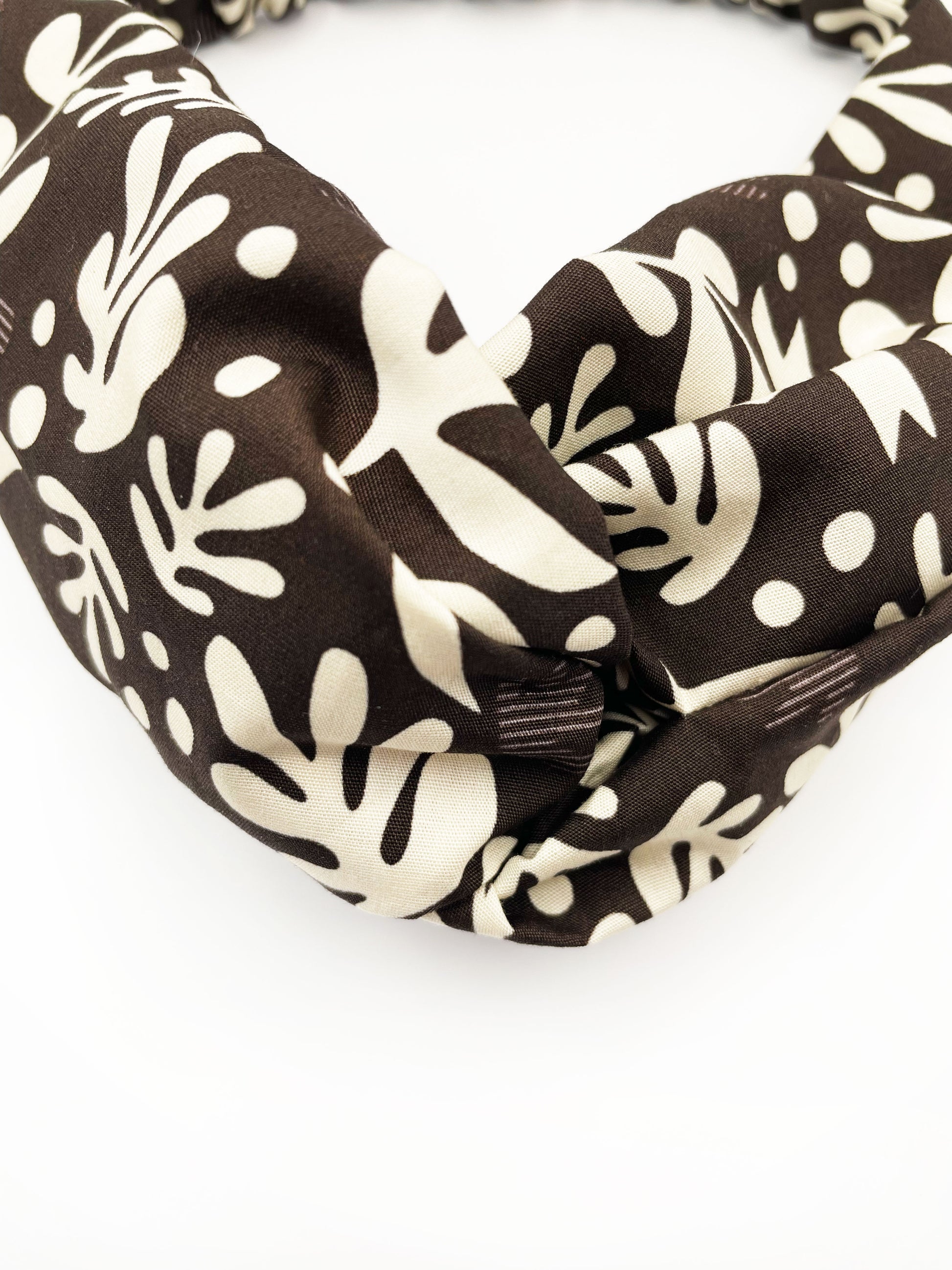 A dark charcoal gray twist headband with cream-colored birds and abstract shapes.