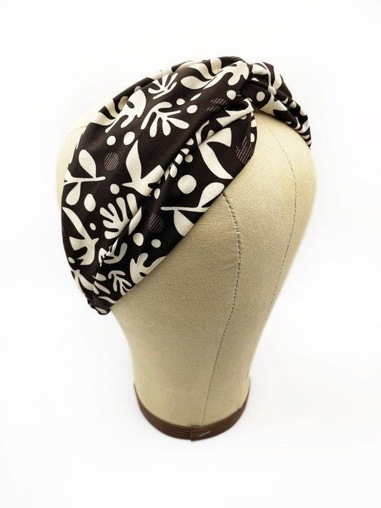 A dark charcoal gray twist headband with cream-colored birds and abstract shapes. The headband is modeled on a mannequin head.