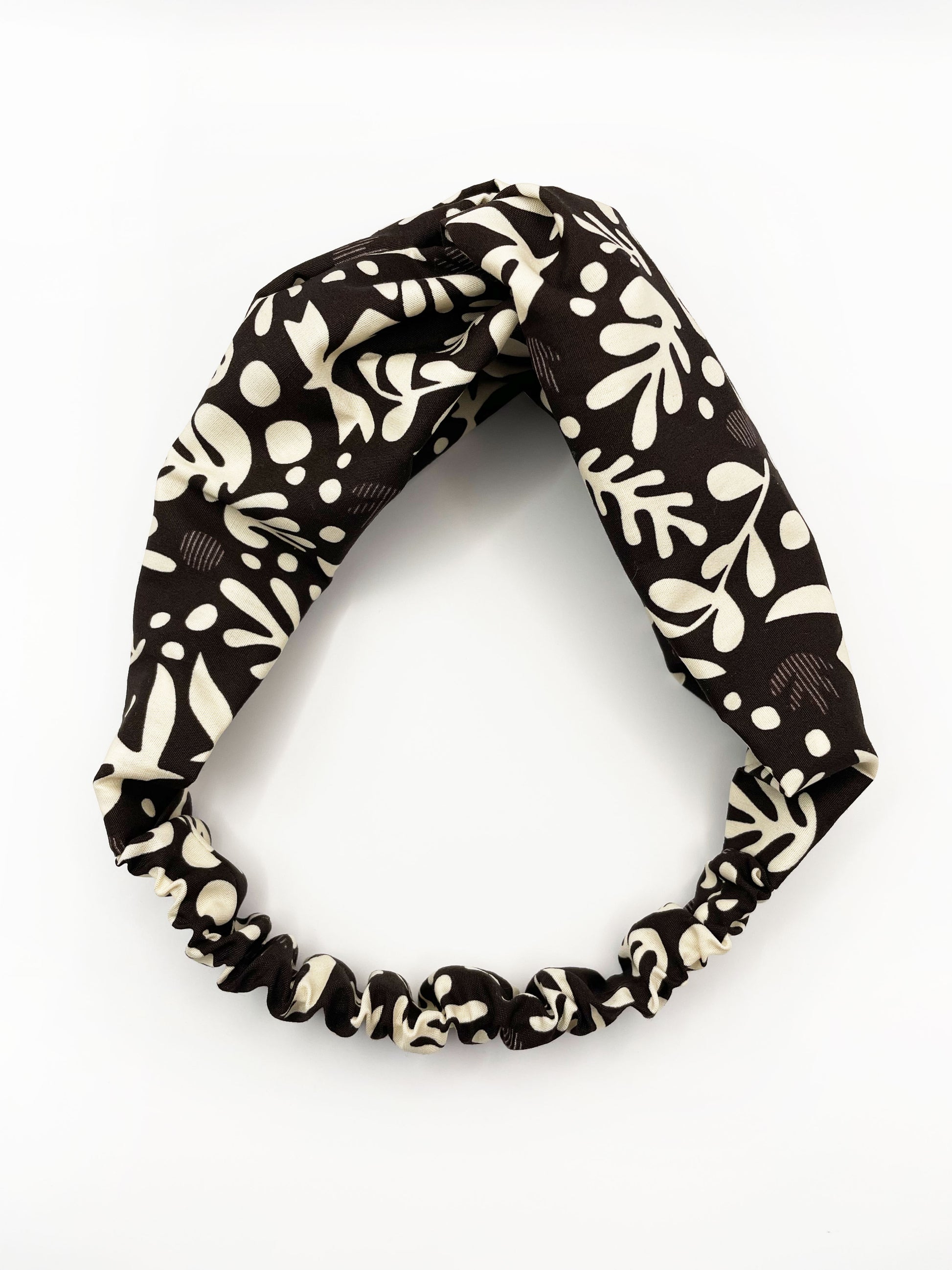 A dark charcoal gray twist headband with cream-colored birds and abstract shapes. The elastic band in the back provides support without slipping.