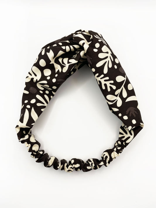 A dark charcoal gray twist headband with cream-colored birds and abstract shapes. The elastic band in the back provides support without slipping.