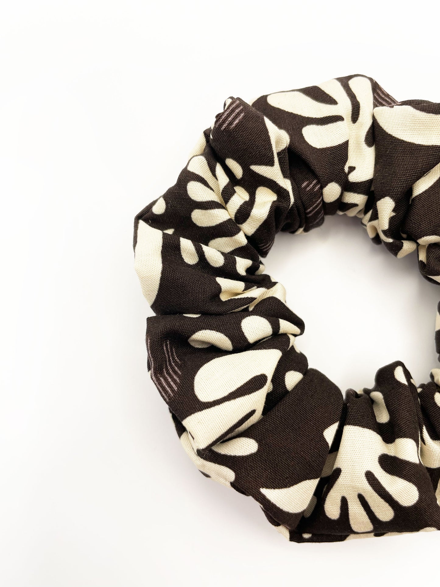 A dark charcoal gray scrunchie with cream-colored birds and abstract shapes. Made with 100% cotton fabric, these scrunchies are gentle on hair and comfortable to wear all day.&nbsp;