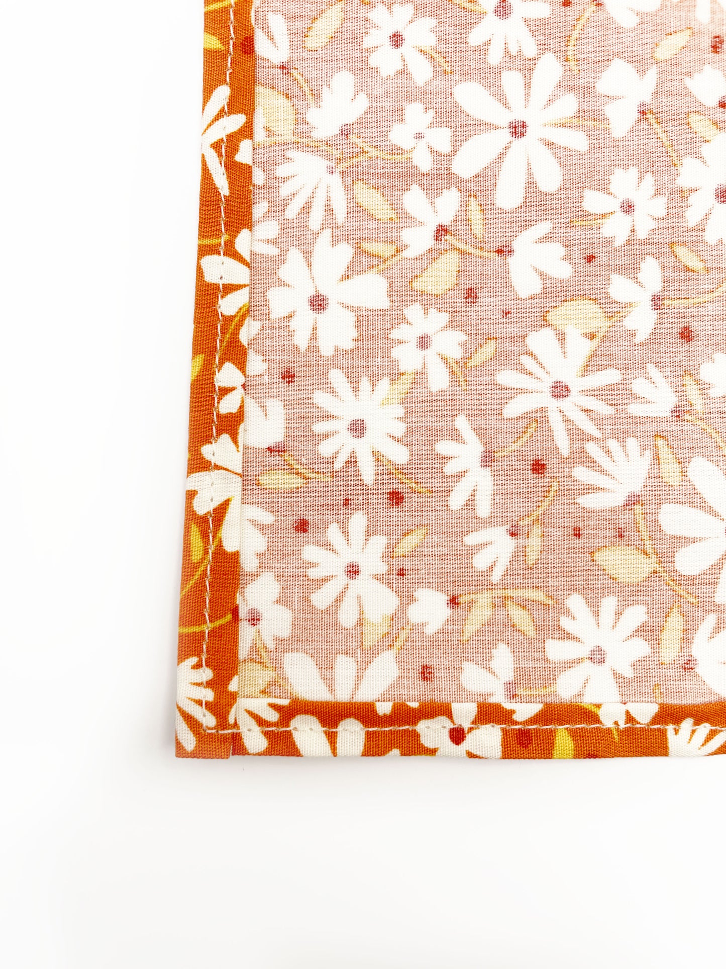 A rust brown floral pocket square with white flowers, showcasing shades of earthy browns and pops of warm peach and blush pink. 