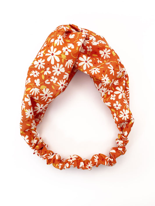 A handmade brown twist headband with off white flowers. The headband has an elastic band on the back.