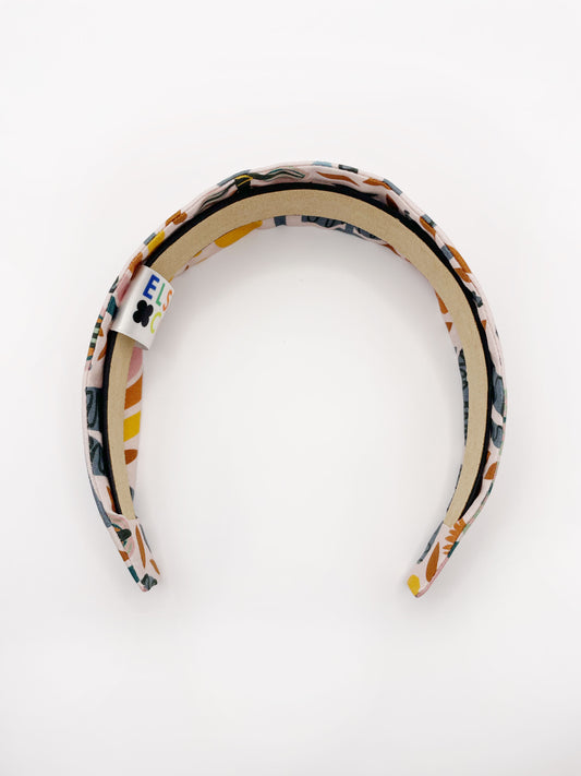 A fabric headband featuring a bold nature-inspired print of bugs, plants, suns, and rainbows. 