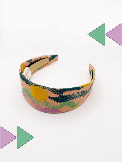 A fabric headband with an abstract design inspired by the desert. The color palette includes sandy brown, soft blue, muted green, and warm terracotta. 