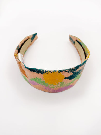 A fabric headband with an abstract design inspired by the desert. The color palette includes sandy brown, soft blue, muted green, and warm terracotta. 