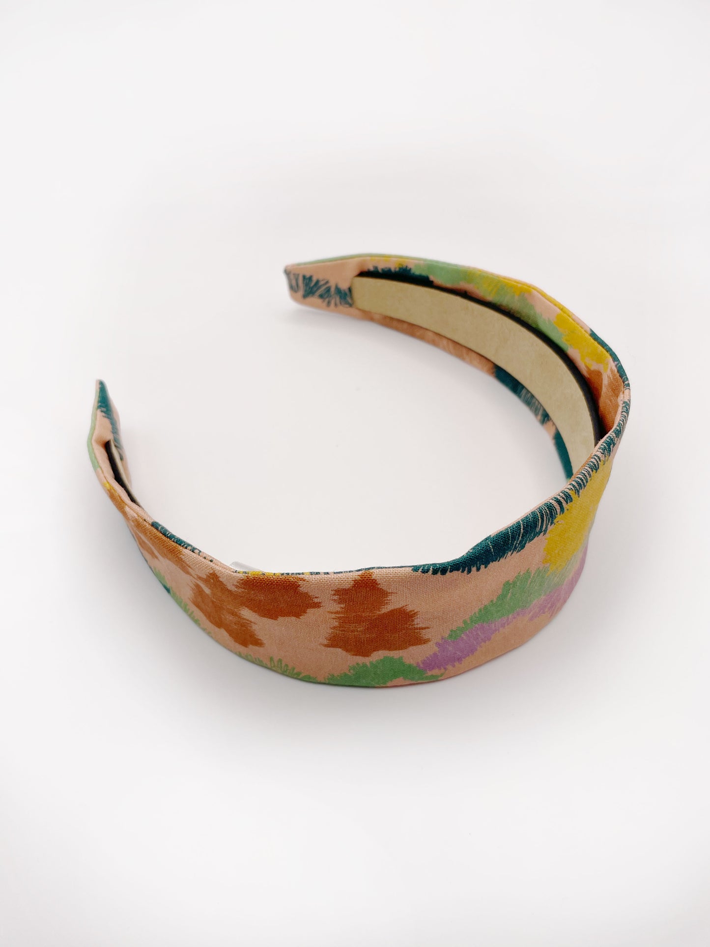 A fabric headband with an abstract design inspired by the desert. The color palette includes sandy brown, soft blue, muted green, and warm terracotta. 