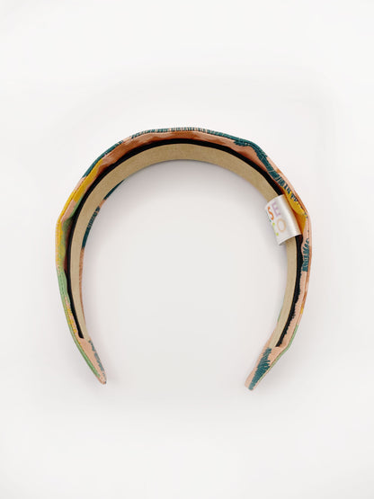 A fabric headband with an abstract design inspired by the desert. The color palette includes sandy brown, soft blue, muted green, and warm terracotta. 