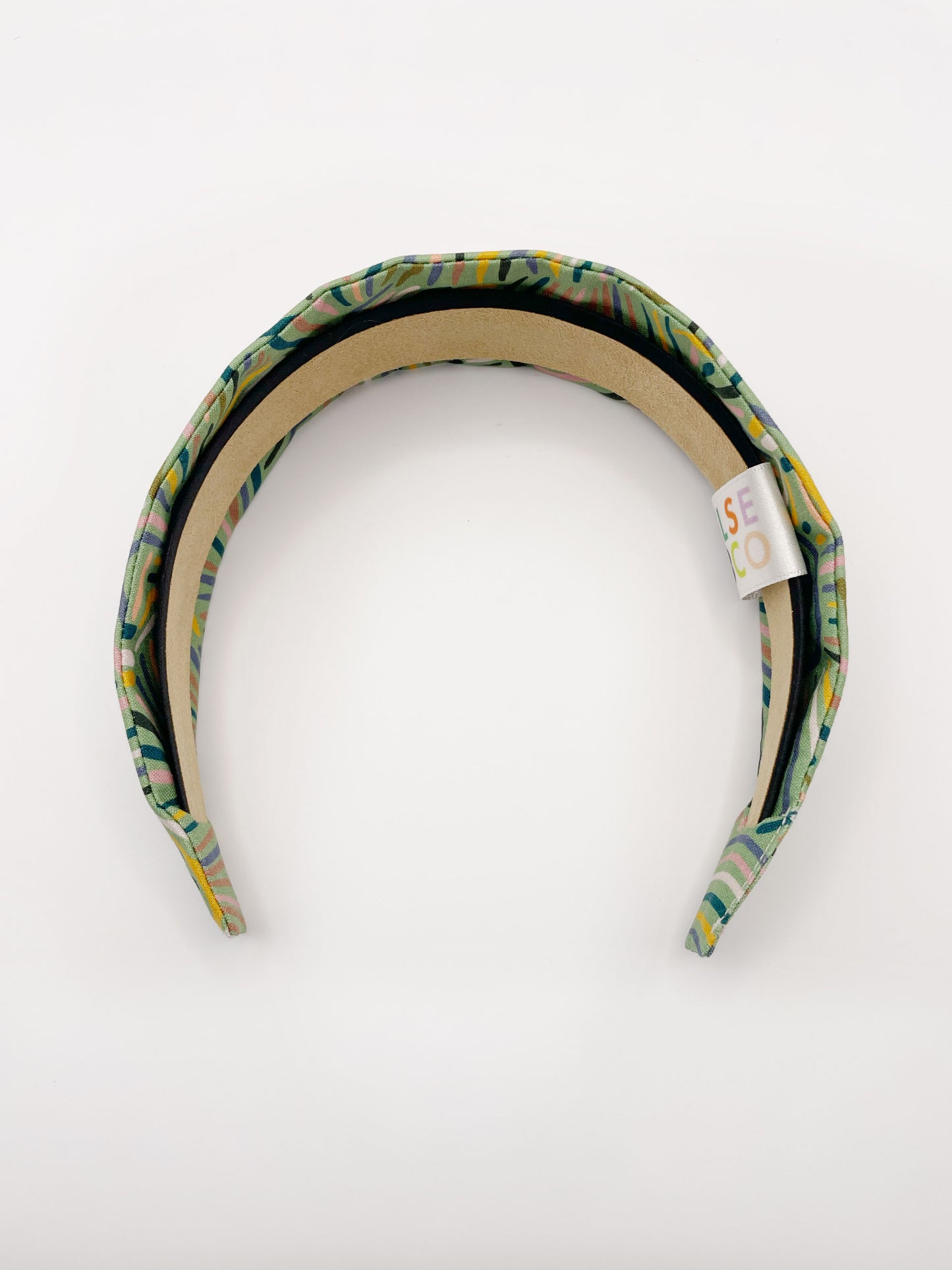 A fabric-covered headband featuring an abstract design inspired by desert rain patterns. The material is green with a soft brushstroke-like print, and a harmonious blend of yellow, pink, and blue.