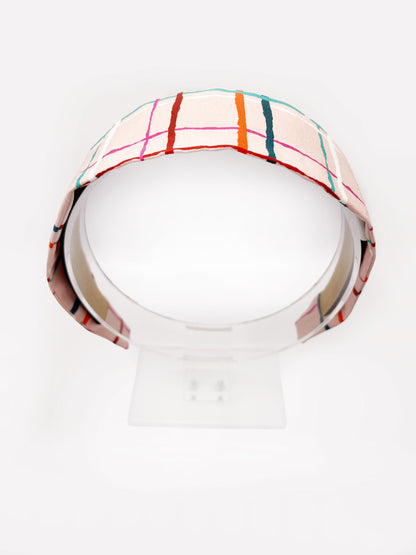 A fabric headband featuring a colorful and modern plaid design with vibrant shades of pink, red, teal, and orange on a soft pastel background. The headband is shown on an acrylic display.