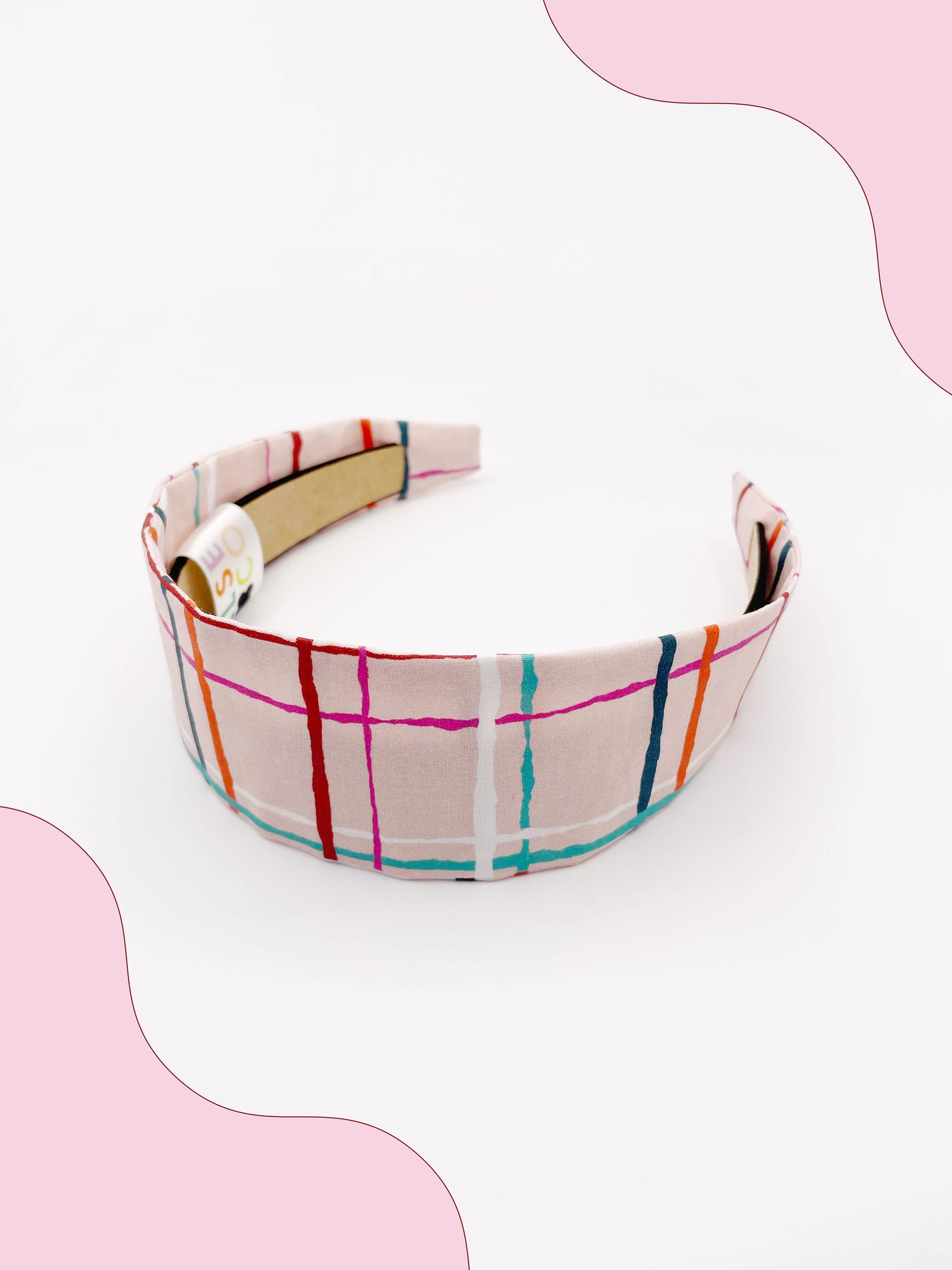 A fabric headband featuring a colorful and modern plaid design with vibrant shades of pink, red, teal, and orange on a soft pastel background.