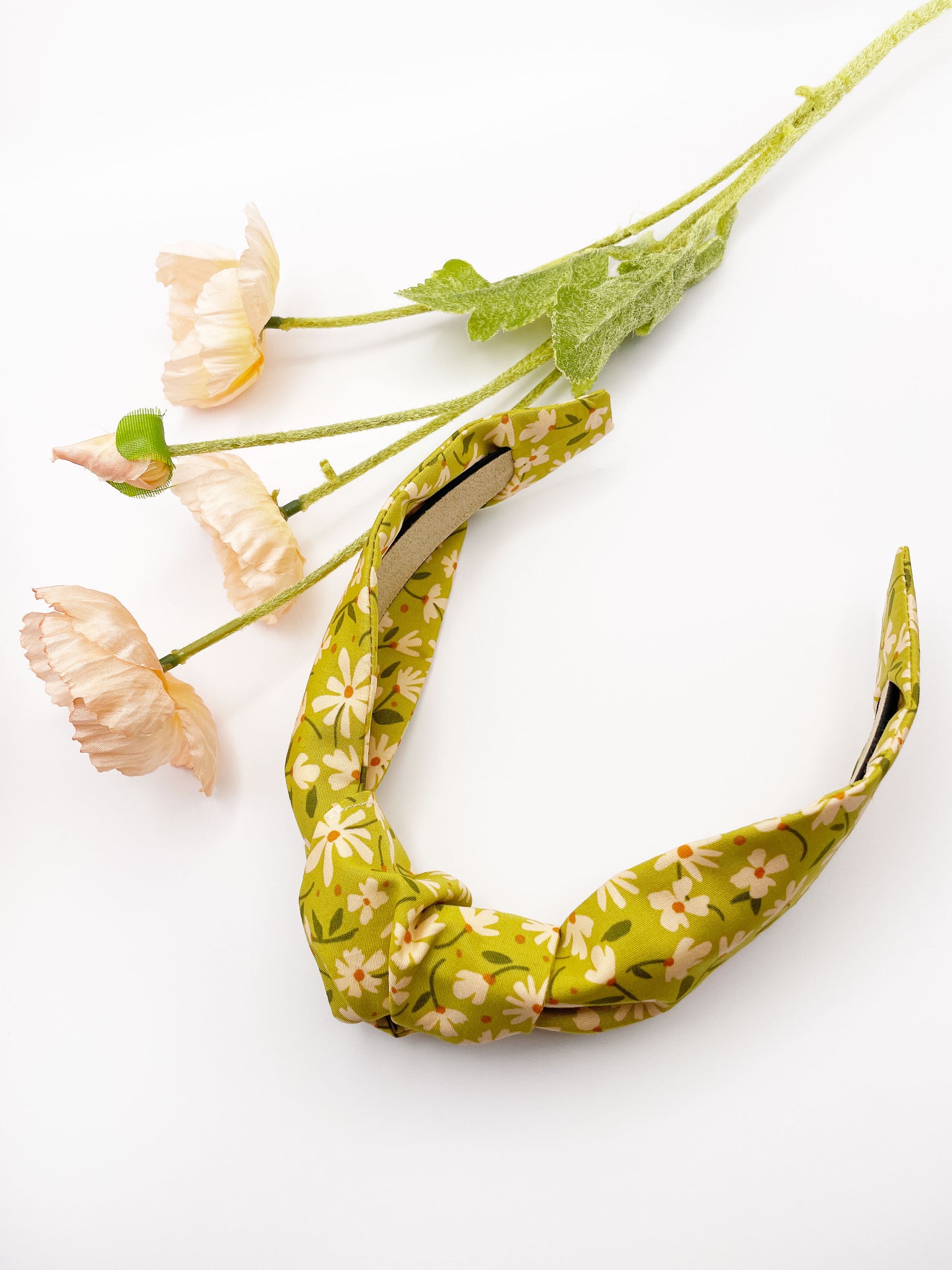 A mossy green knotted headband with cream flowers, showcasing shades of earthy browns and pops of warm peach and blush pink.