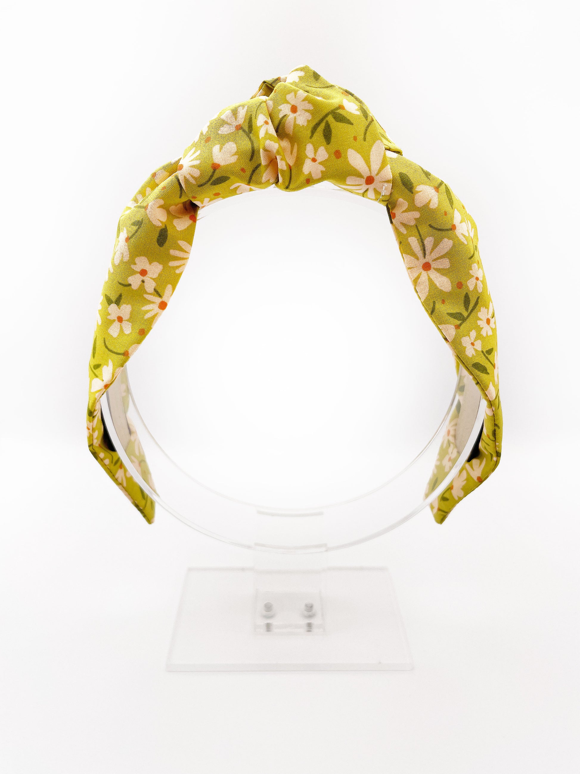 A mossy green knotted headband with cream flowers, showcasing shades of earthy browns and pops of warm peach and blush pink.