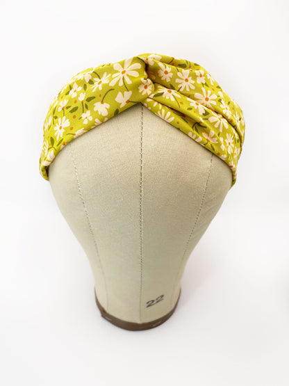 A handmade green twist headband with off white flowers. The headband is modeled on a mannequin head.