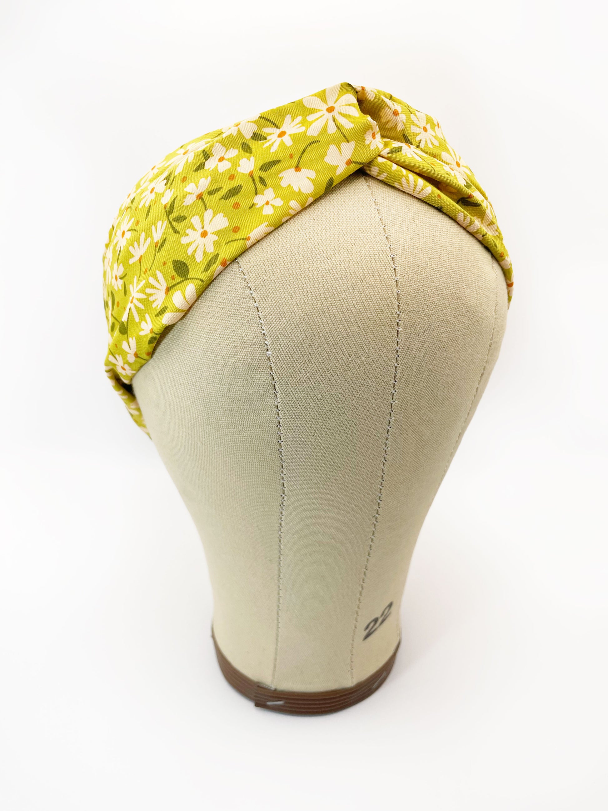 A handmade green twist headband with off white flowers. The headband is modeled on a mannequin head.