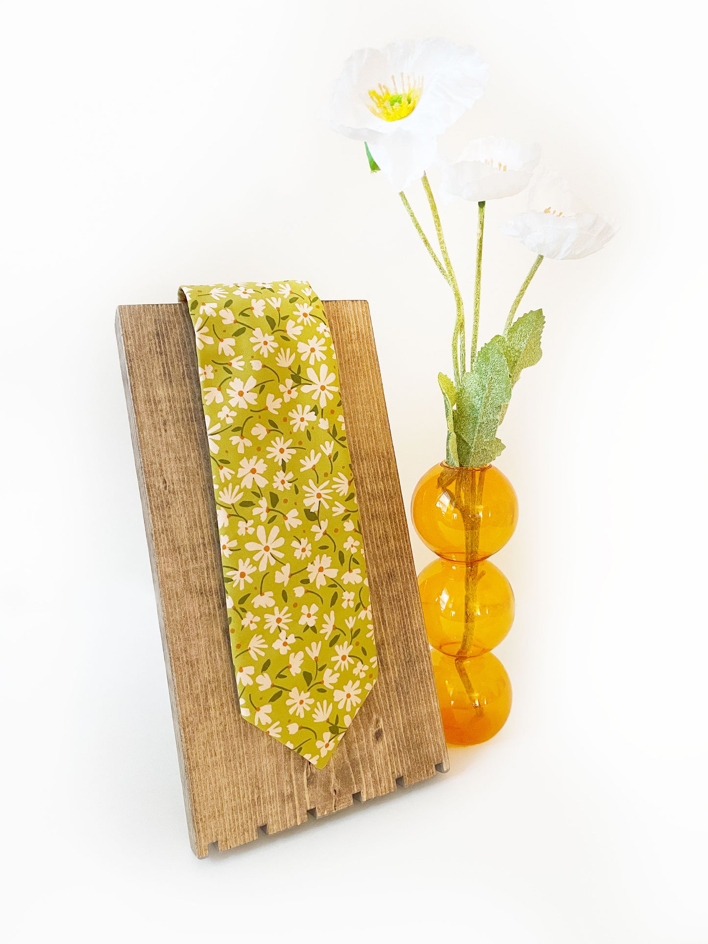 A mossy green handmade necktie with cream flowers, showcasing shades of earthy browns and pops of warm peach and blush pink.