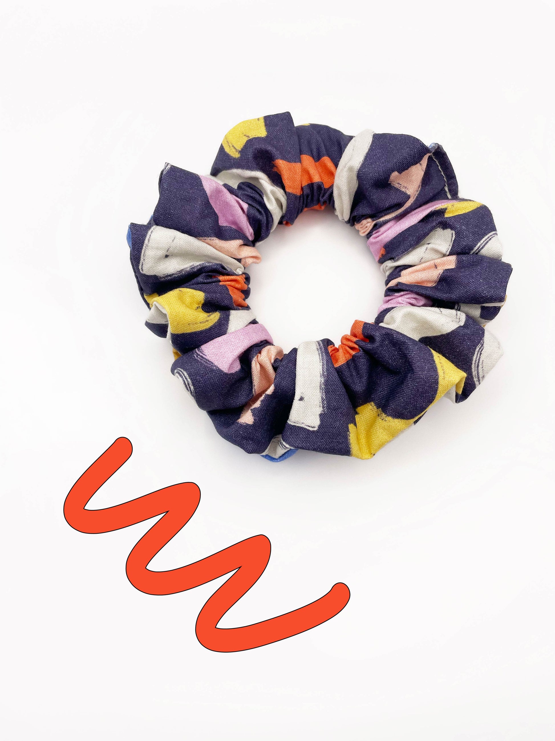 A navy blue scrunchie with a colorful abstract print featuring various doodles. Wear this hair tie on your wrist, or use it as a bun or ponytail holder.