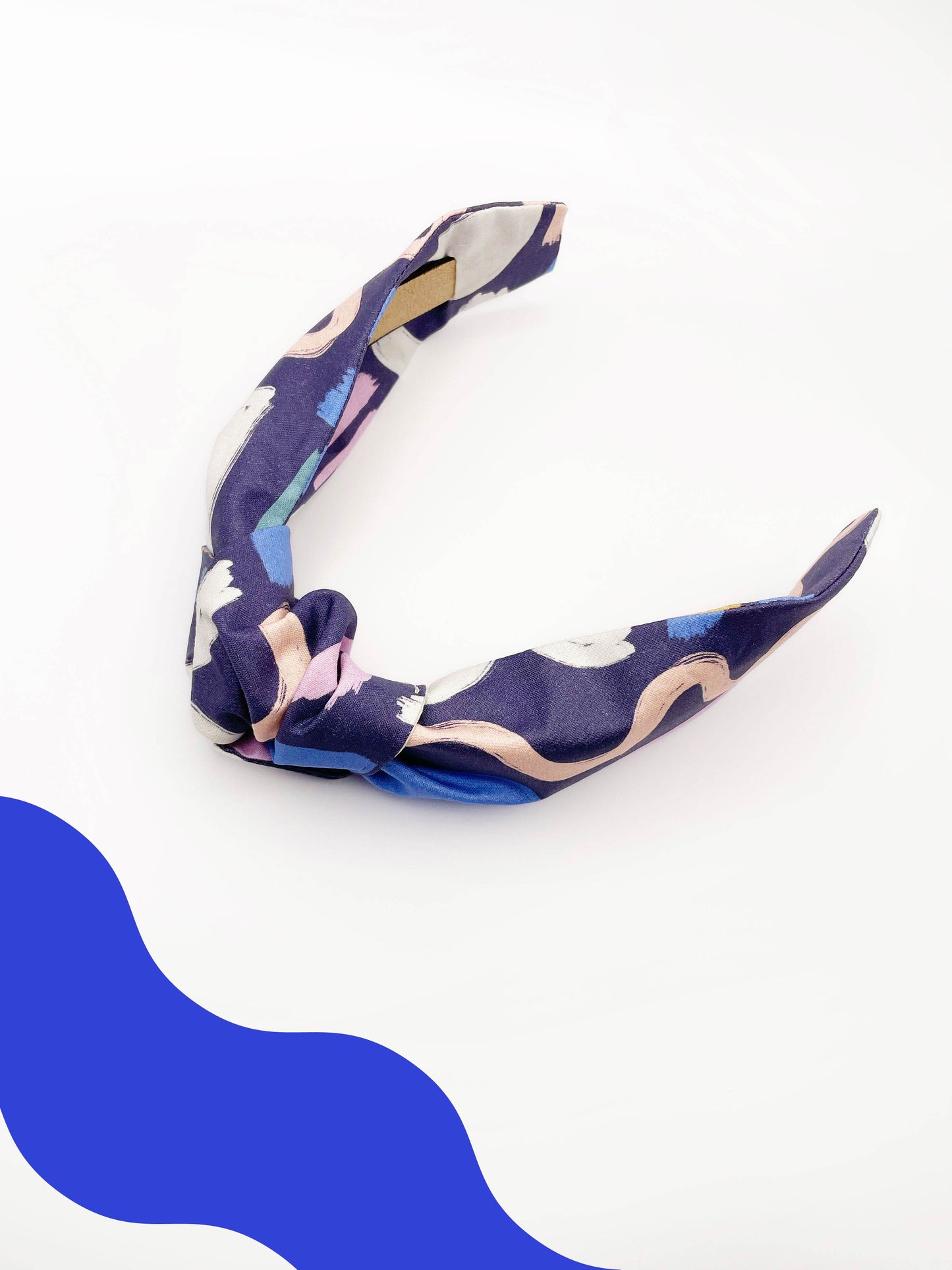 A navy blue knotted headband with a colorful abstract print featuring various doodles. Each headband is crafted with cotton fabric attached to a durable hair band for a secure and comfortable fit.