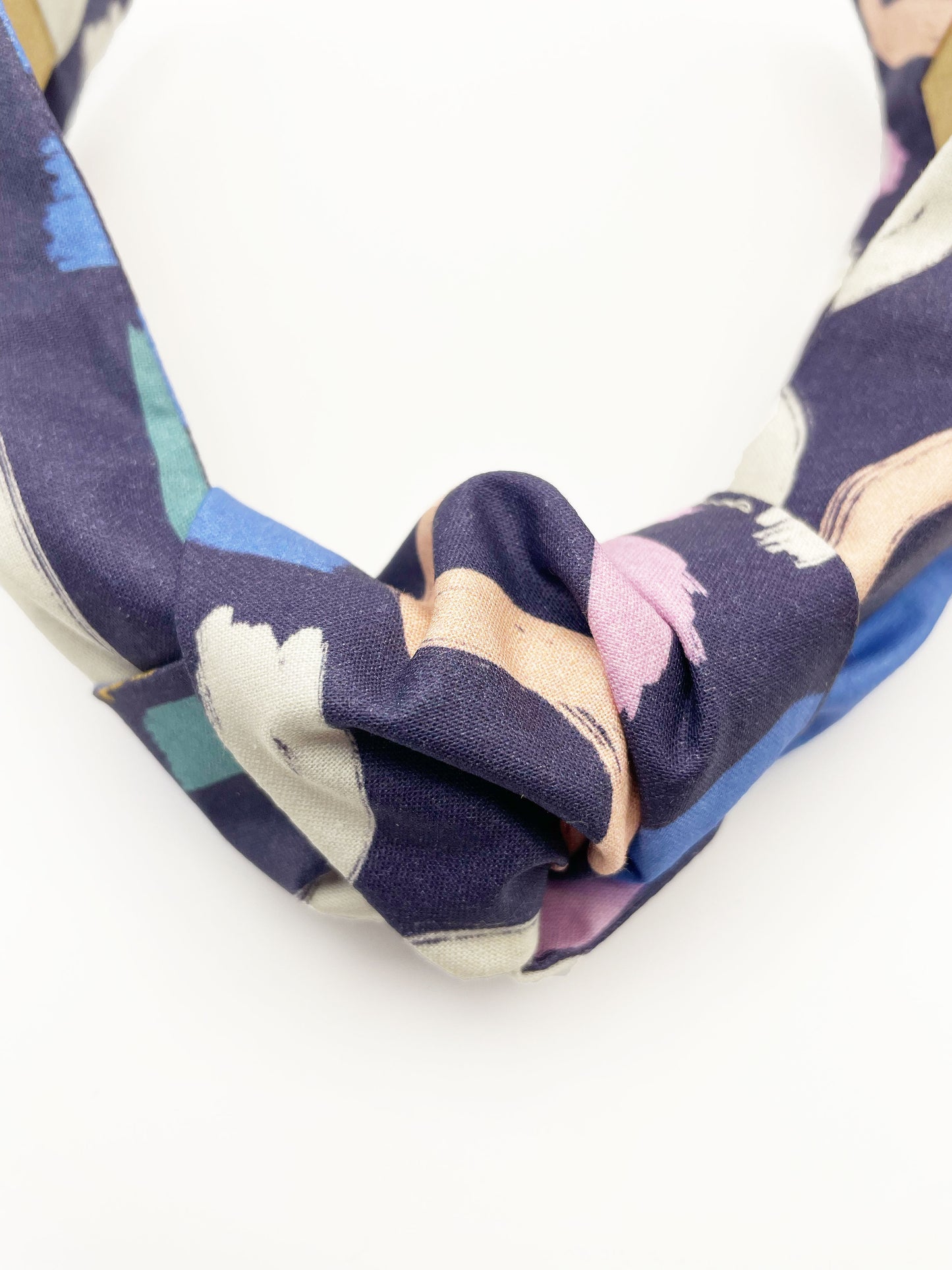 A navy blue knotted headband with a colorful abstract print featuring various doodles. Each headband is crafted with cotton fabric attached to a durable hair band for a secure and comfortable fit.